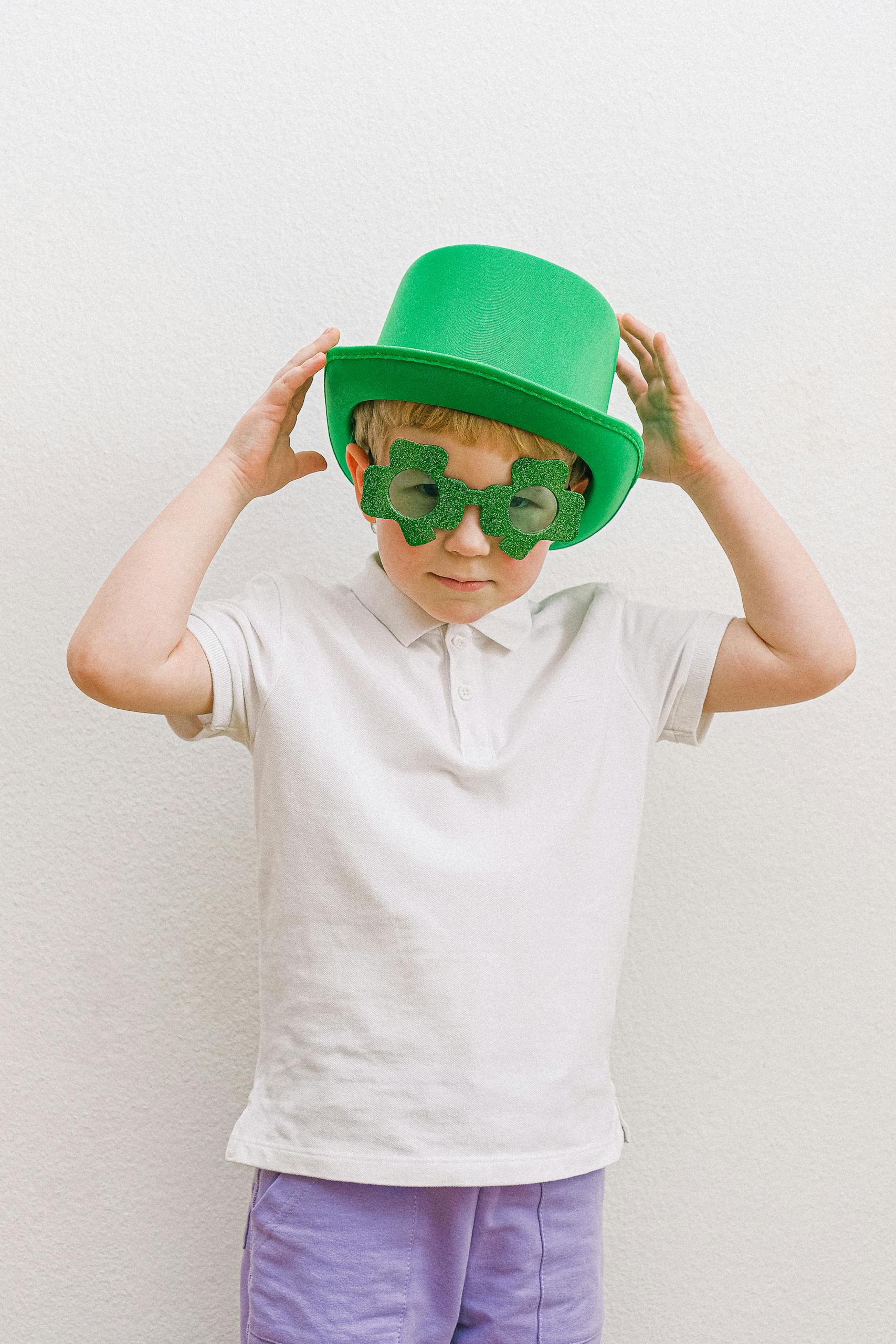 A young boy in a green hat and glasses celebrating St. Patrick's Day.